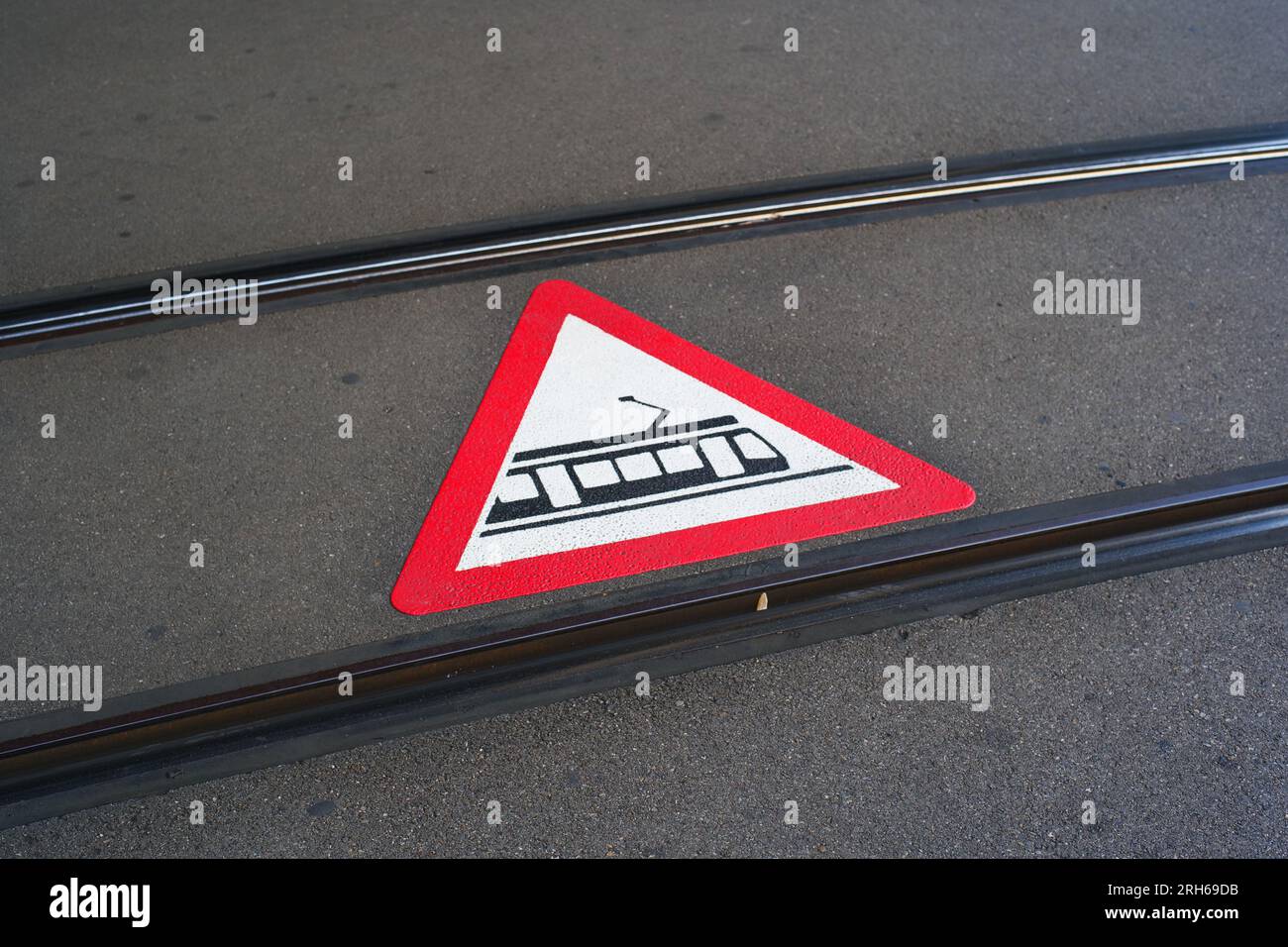 Cartello di avvertimento o pittogramma di attraversamento del tram dipinto sulla strada asfaltata tra i binari dei treni in una città in Europa. Niente persone. Foto Stock