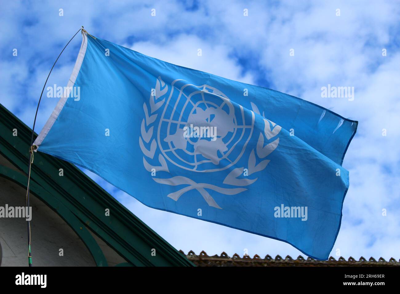 Bandiera ONU che sventola nel vento di fronte a un cielo blu con nuvole bianche. Emblema ufficiale delle Nazioni Unite. Concetto di pace nel mondo Foto Stock