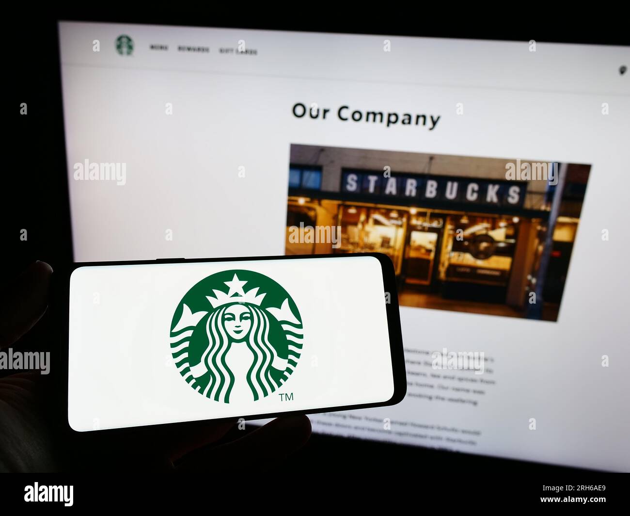 Persona che possiede uno smartphone con il logo della società statunitense Starbucks Corporation sullo schermo davanti al sito Web. Concentrarsi sul display del telefono. Foto Stock