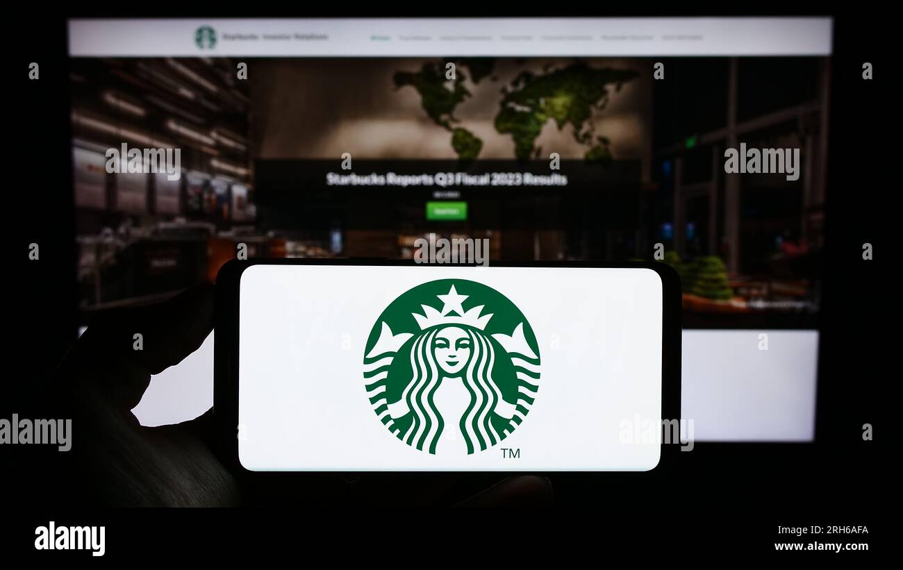 Persona che tiene il cellulare con il logo dell'azienda americana Starbucks Corporation sullo schermo davanti alla pagina Web. Concentrarsi sul display del telefono. Foto Stock