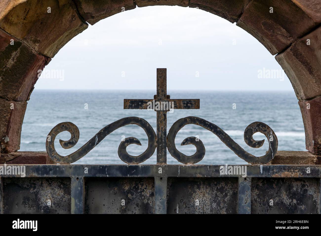 Misterioso cancello in metallo del cimitero con sfondo a croce e skyline marino Foto Stock