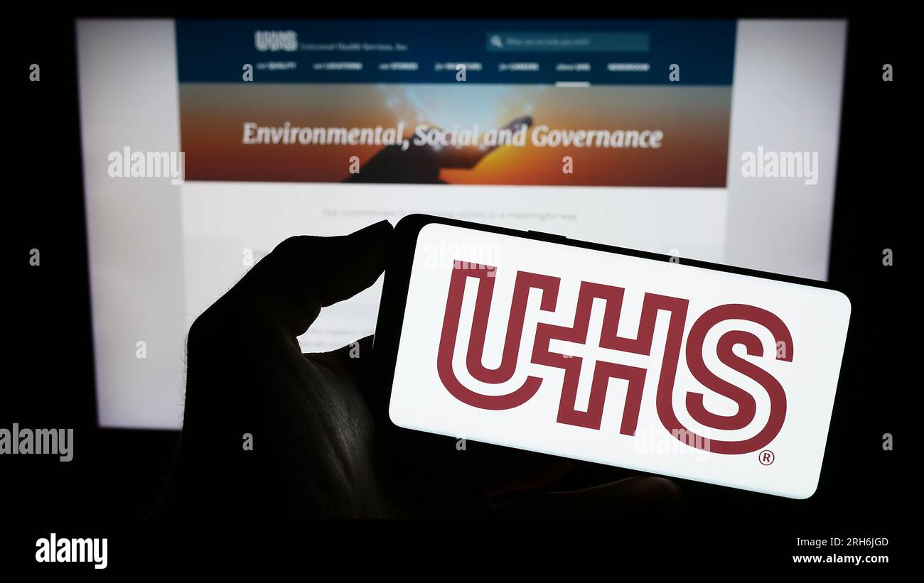 Persona in possesso di cellulare con logo della società statunitense Universal Health Services Inc (UHS) sullo schermo davanti alla pagina Web. Concentrarsi sul display del telefono. Foto Stock