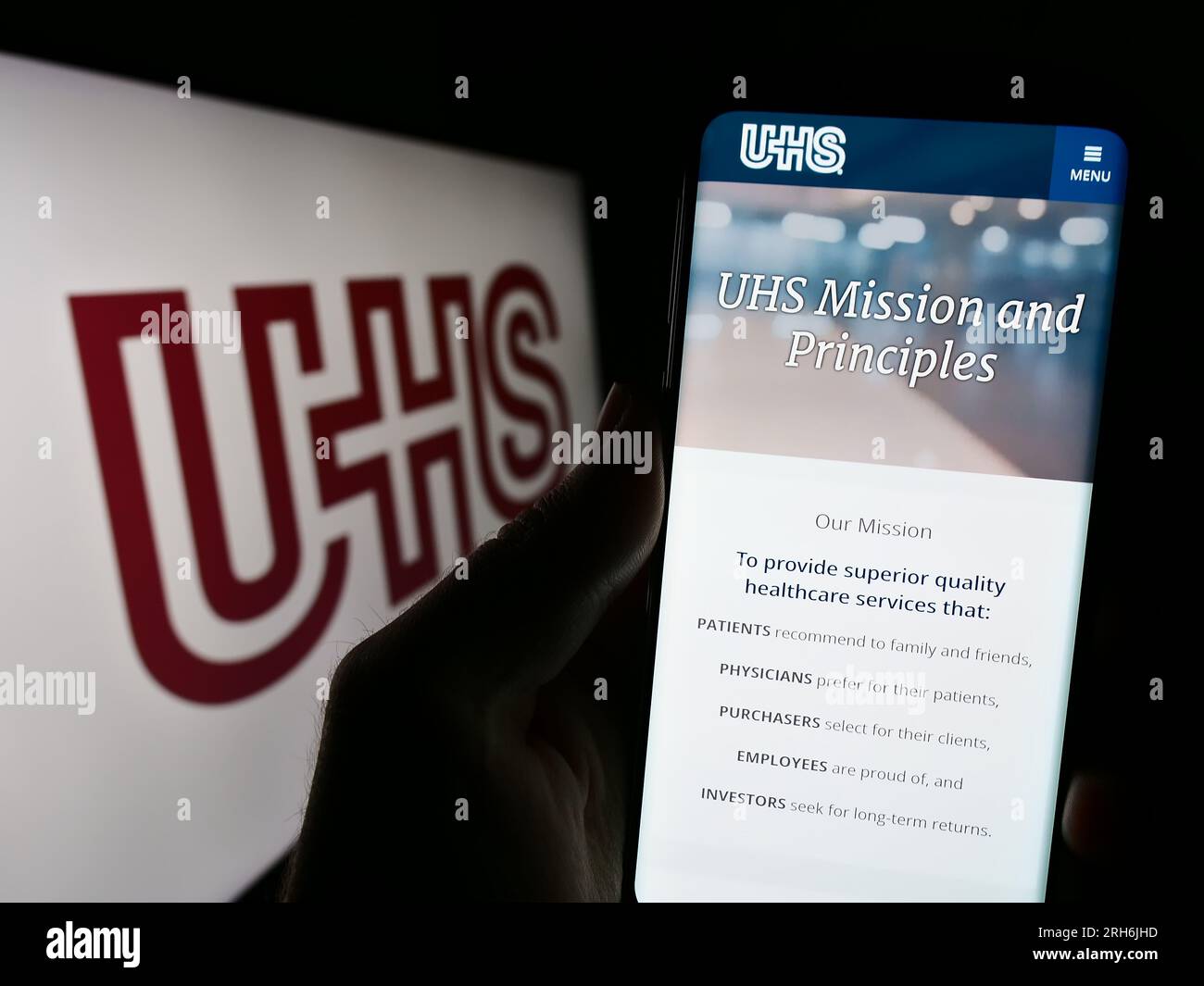 Persona in possesso di cellulare con pagina web della società statunitense Universal Health Services Inc. (UHS) sullo schermo davanti al logo. Concentrarsi sul centro del display del telefono. Foto Stock