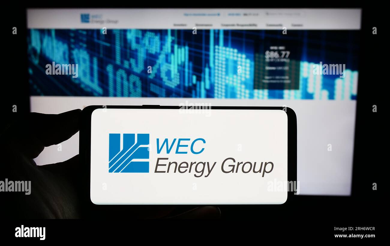 Persona che possiede il cellulare con il logo della società di servizi pubblici statunitense WEC Energy Group Inc. Sullo schermo davanti alla pagina Web aziendale. Concentrarsi sul display del telefono. Foto Stock