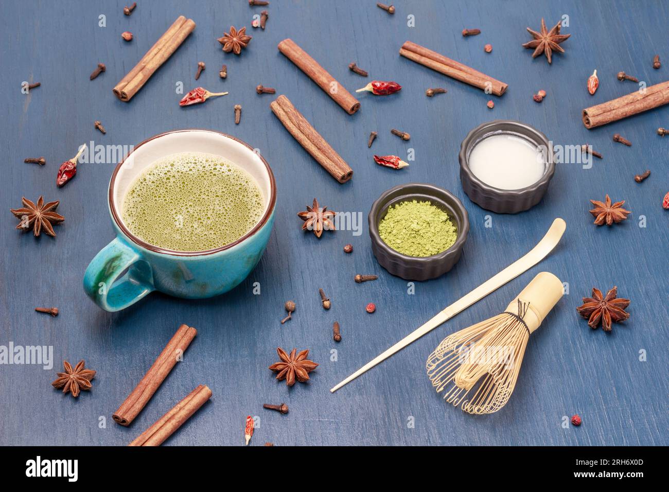 Tè Matcha in una tazza blu, latte e tè Matcha in polvere. Spezie sul tavolo. Sfondo blu Foto Stock