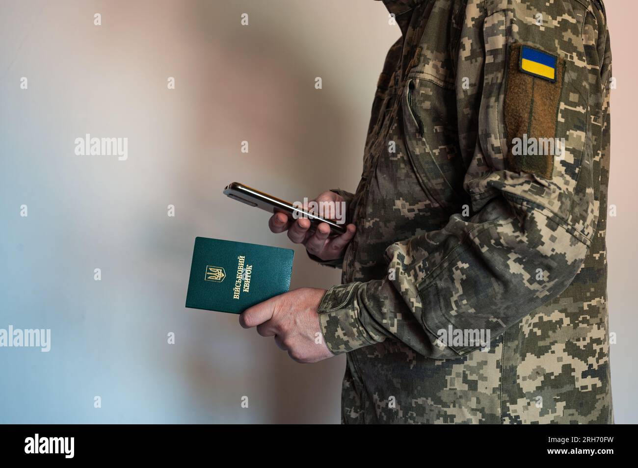 Soldato in tuta tattica tiene in mano un documento di identità militare e scatta foto con lo smartphone. Uniforme pixel Ucraina Foto Stock