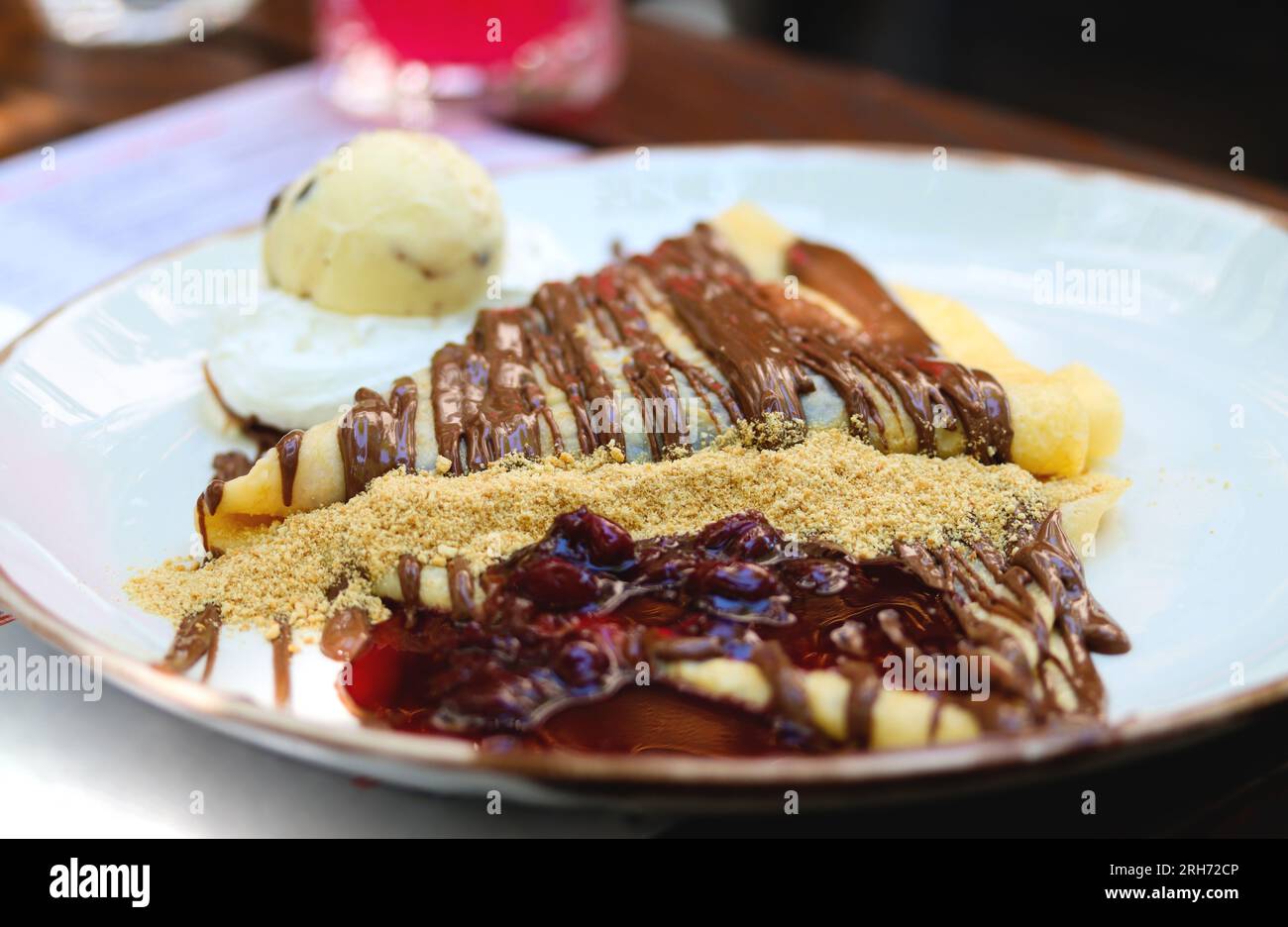 Crepes con crema al cioccolato. Pancake con pasta al cioccolato, nocciole, salsa di ciliegia e una paletta di gelato su un piatto bianco su un tavolo del ristorante. T Foto Stock