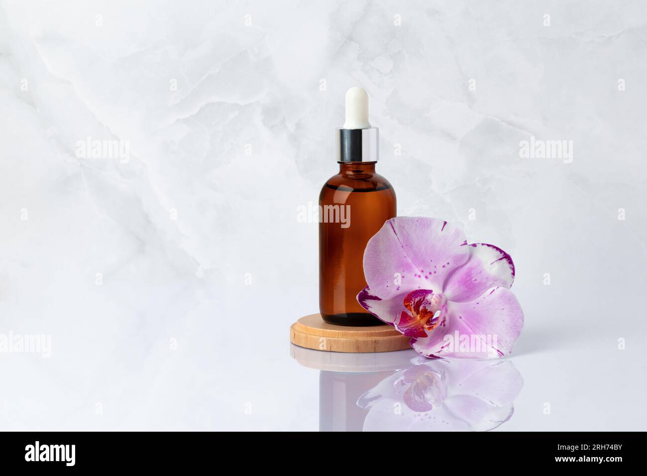 Bottiglia di vetro marrone su podio di legno e fiore di orchidea rosa da vicino. Olio aromatico per massaggi su fondo di marmo grigio con riflesso. S organico naturale Foto Stock