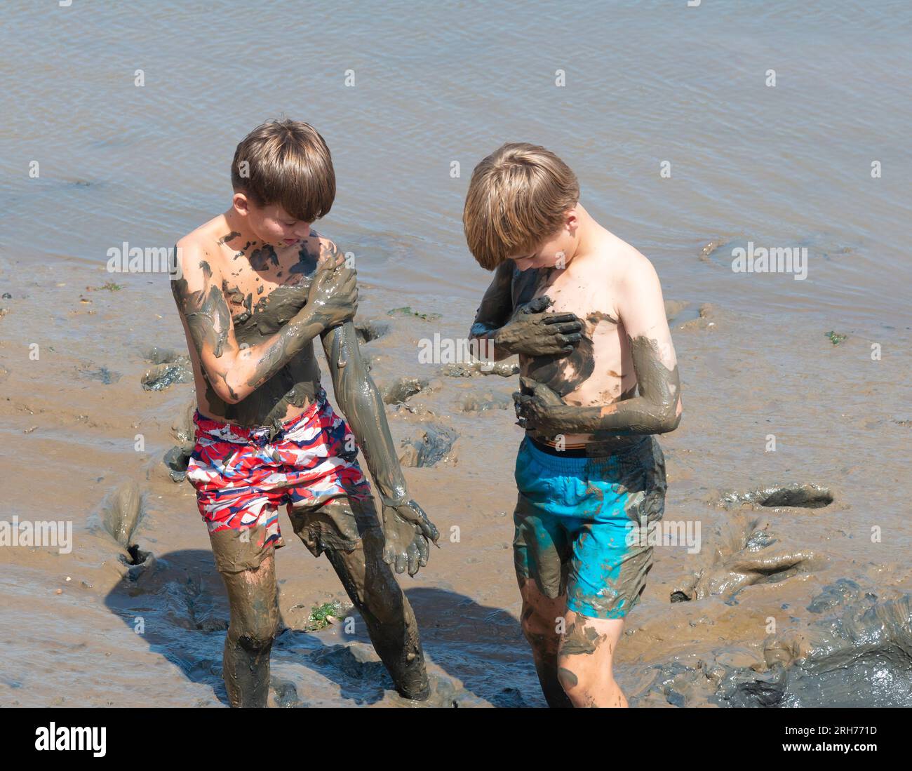 Due ragazzi che giocano e si divertono a coprirsi di fango vicino al mare nel Norfolk settentrionale, Inghilterra, Regno Unito Foto Stock