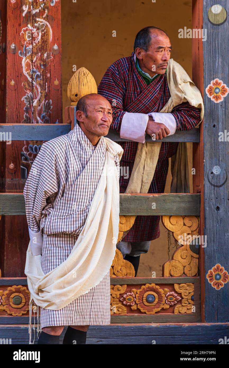 TONGSA, BHUTAN - 3 GENNAIO 2023: Uomini bhutansi che indossano il tradizionale Gho osservano il locale Tshechu Foto Stock