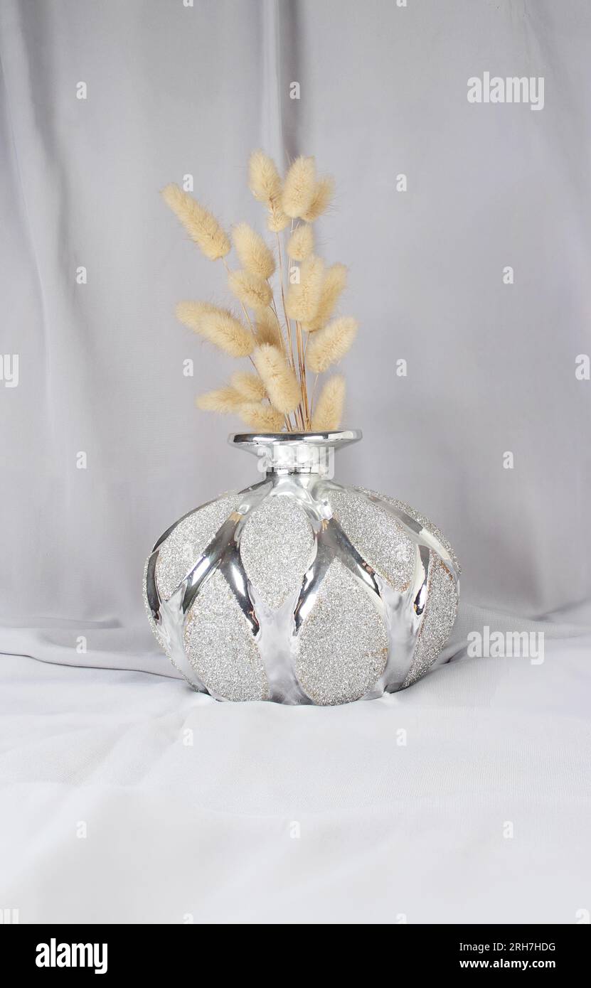Erba a coda di coniglio asciutta decorativa in vaso luminoso su tessuto grigio. Scatto verticale. Idea di decorazione. Foto Stock