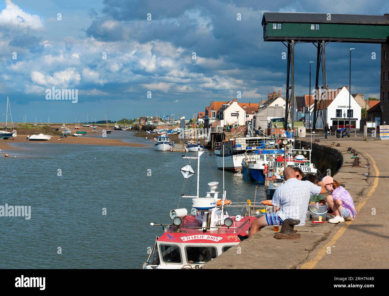 La famiglia si imbarca sulla banchina nella città di villeggiatura di Wells-Next-the-Sea con le sue barche da pesca ormeggiate lungo la bassa marea. Norfolk, Inghilterra Foto Stock