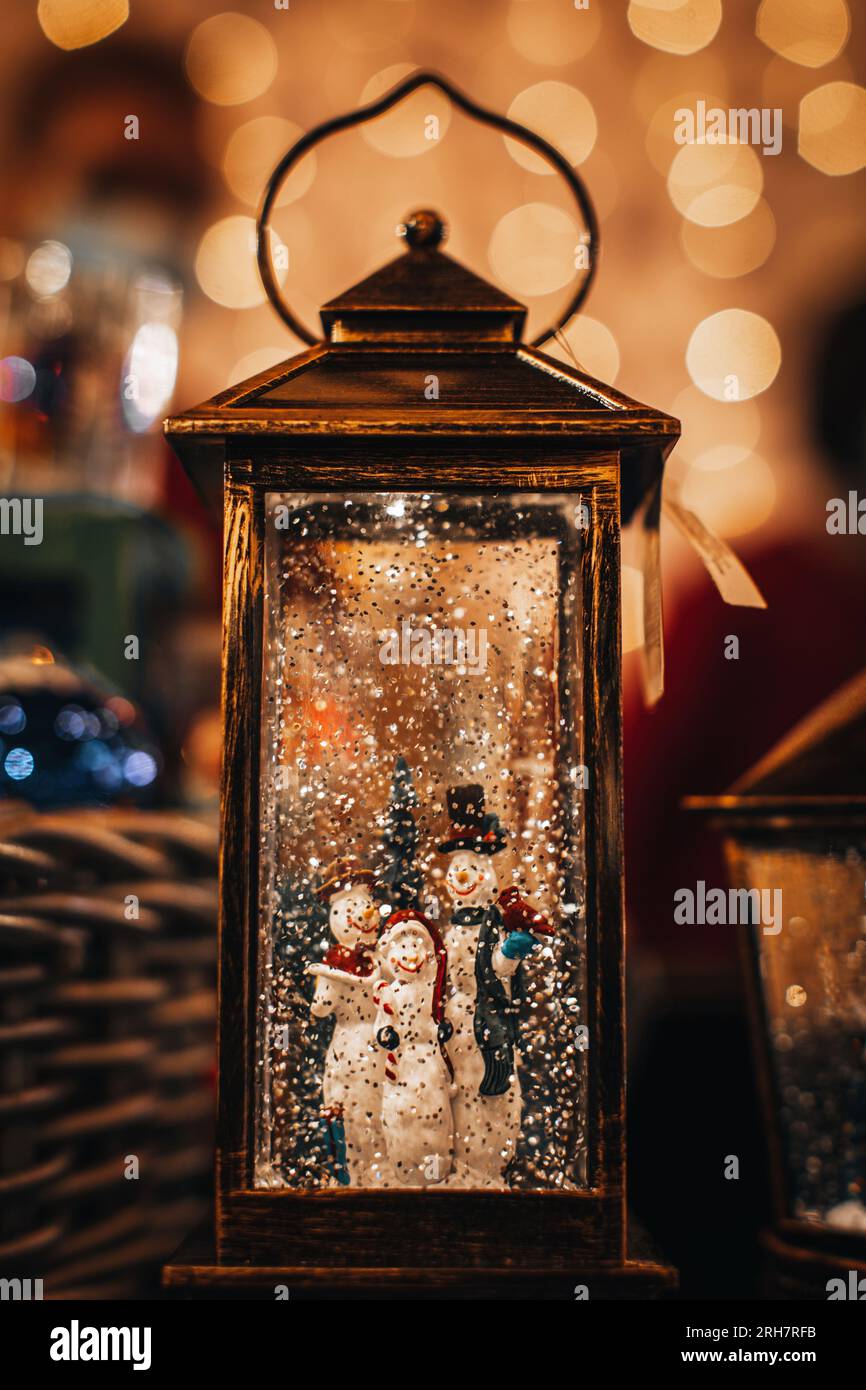 Lanterna magica composizione invernale festiva con i pupazzi di neve della famiglia dei cartoni animati. Installazione di Capodanno per le vacanze natalizie con luci bokeh dorate Foto Stock