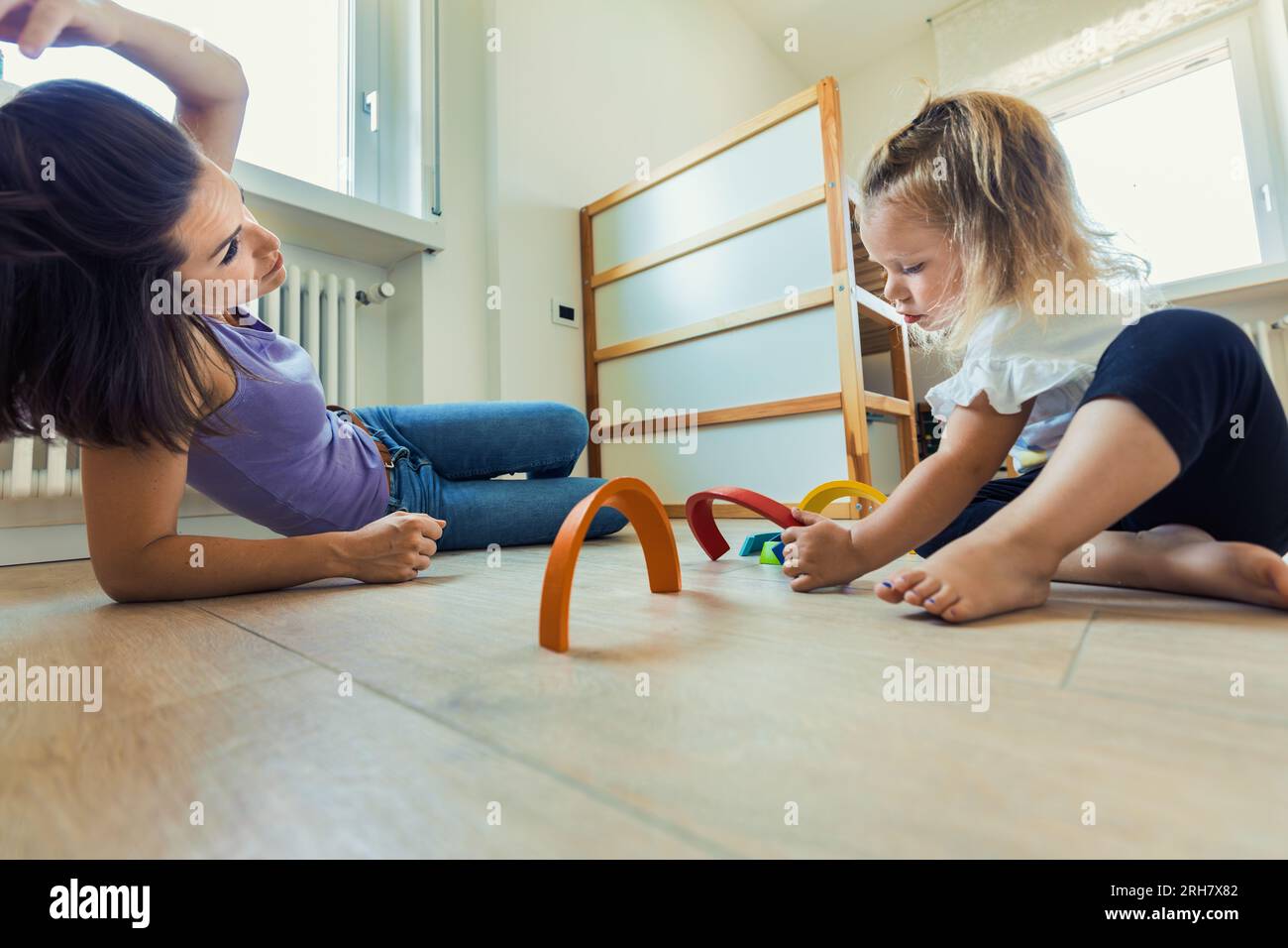 All'interno di una stanza piena di giocattoli di legno, i momenti madre-figlia fioriscono mentre giocano, sperimentano e imparano insieme Foto Stock