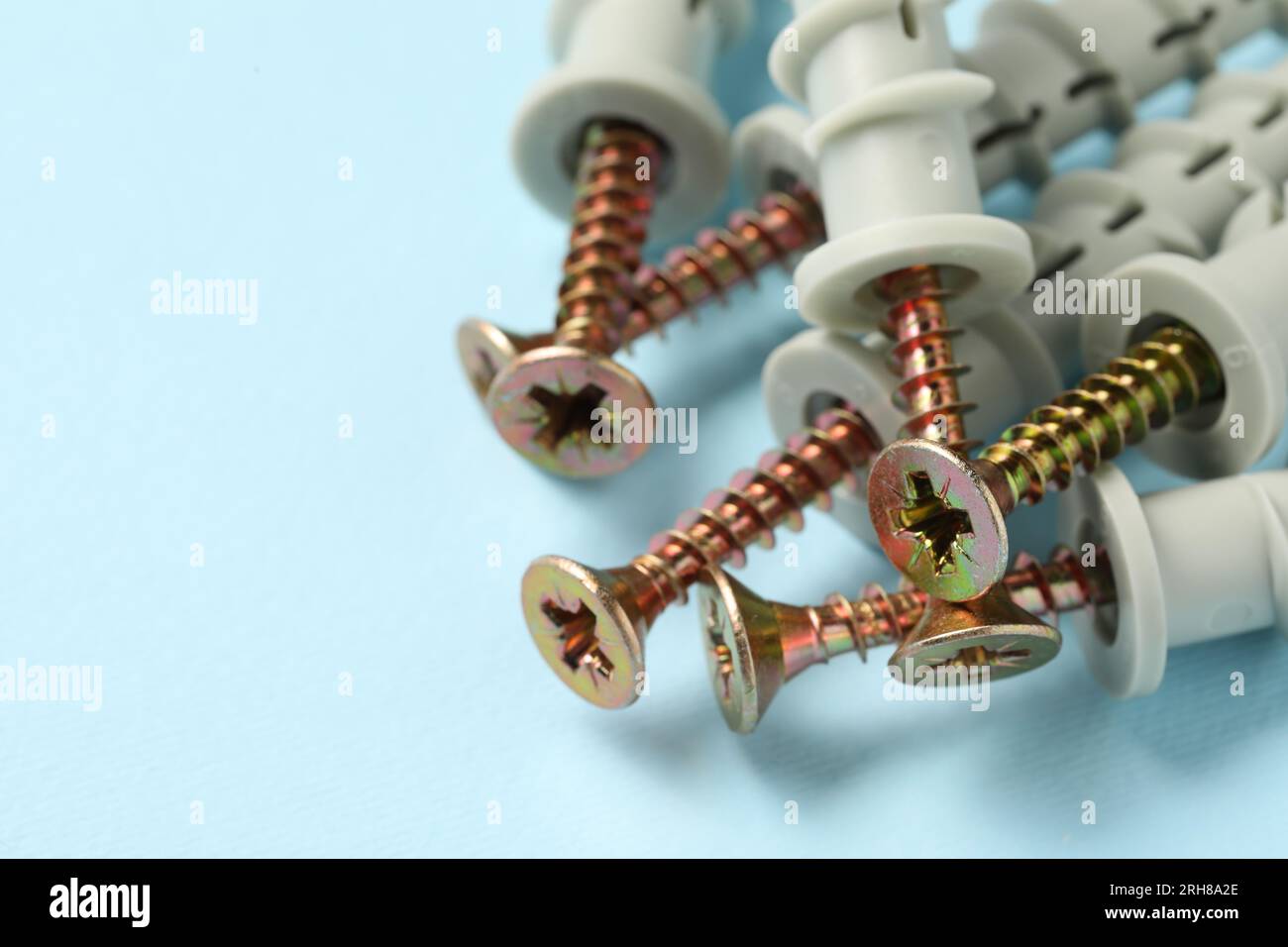 Molte viti metalliche con tasselli su sfondo azzurro, primo piano. Spazio per il testo Foto Stock