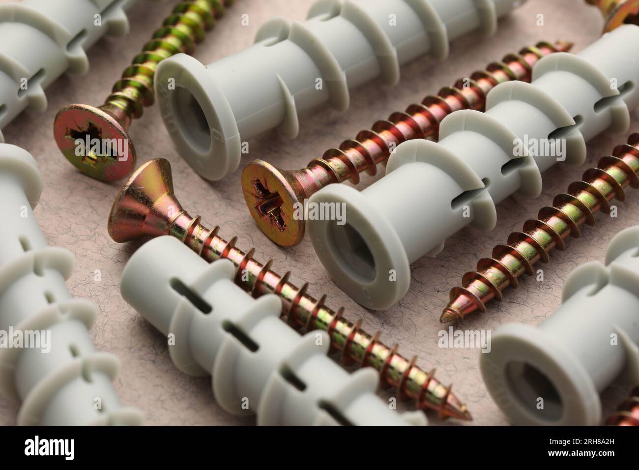 Molte viti e tasselli in metallo sul tavolo beige, primo piano Foto Stock
