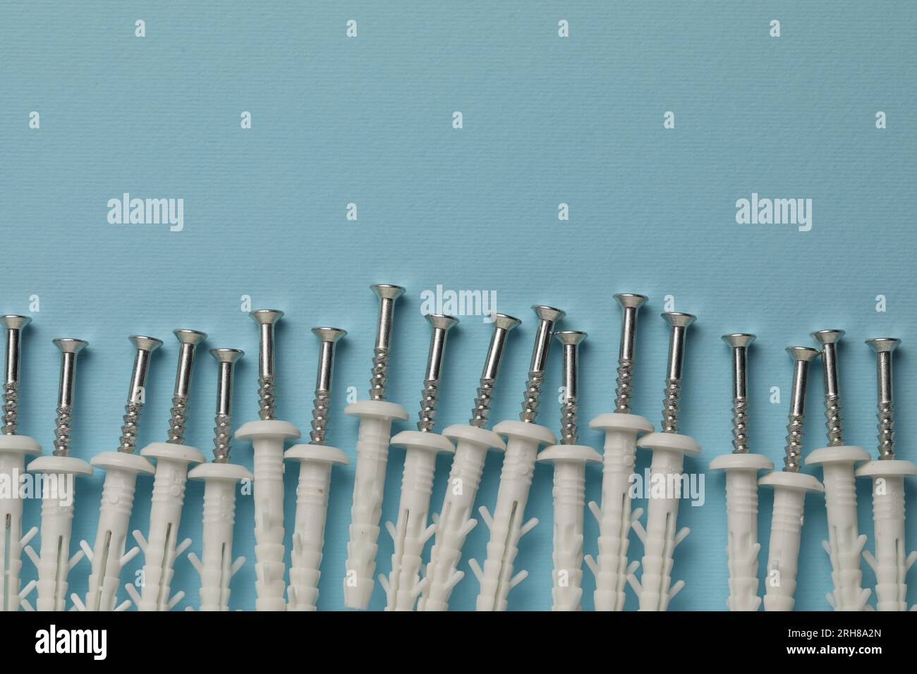 Molte viti in metallo con tasselli bianchi su sfondo azzurro, posizionamento piatto. Spazio per il testo Foto Stock
