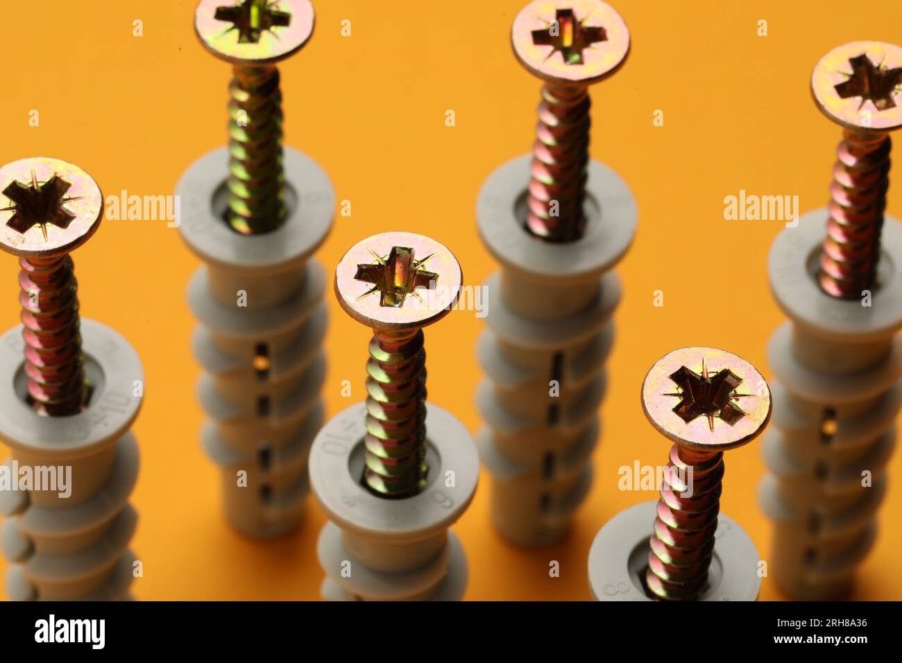 Molte viti metalliche con perni su sfondo arancione, primo piano Foto Stock