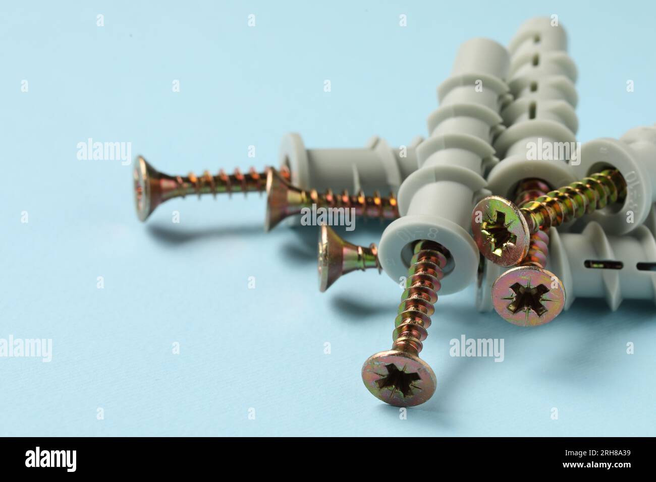 Molte viti metalliche con tasselli su sfondo azzurro, primo piano. Spazio per il testo Foto Stock
