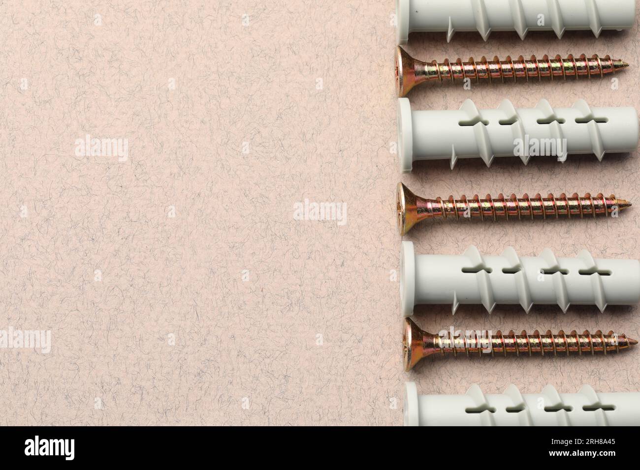 Molte viti e tasselli in metallo su un tavolo ruvido beige, posizionamento piatto. Spazio per il testo Foto Stock