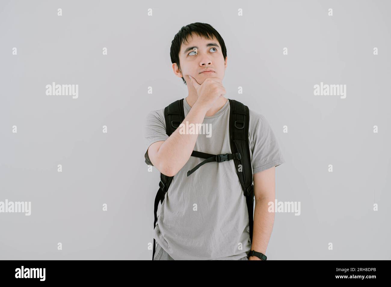 La messa a fuoco selettiva di un giovane asiatico che indossa una maglietta casual verde salvia, uno smartwatch e uno zaino è confuso e guarda il lato superiore destro Foto Stock La messa a fuoco selettiva di un giovane asiatico che indossa una maglietta casual verde salvia, uno smartwatch e uno zaino è confuso e guarda il lato superiore destro Foto Stock