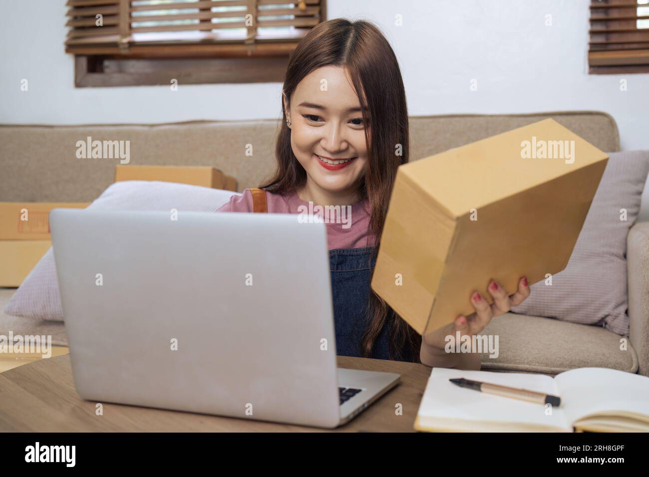 Giovane donna d'affari che lavora online e-commerce a casa. Una giovane donna venditrice prepara una scatola di prodotti da consegnare al cliente Foto Stock