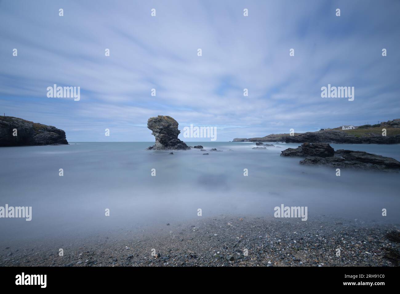 Una piccola pila di roccia appena fuori da una spiaggia di ciottoli nel Galles. L'esposizione prolungata conferisce al mare un aspetto liscio e setoso. Foto Stock