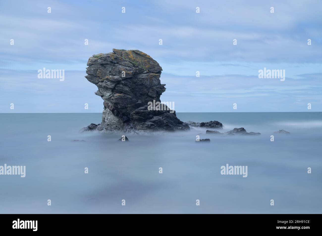 Una piccola pila di roccia appena fuori da una spiaggia di ciottoli nel Galles. L'esposizione prolungata conferisce al mare un aspetto liscio e setoso. Foto Stock