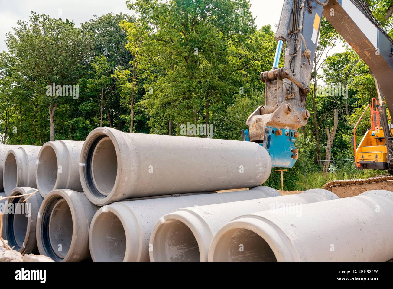 Tubi in calcestruzzo di grande diametro per lavori di drenaggio consegnati in cantiere e scaricati dall'escavatore Foto Stock