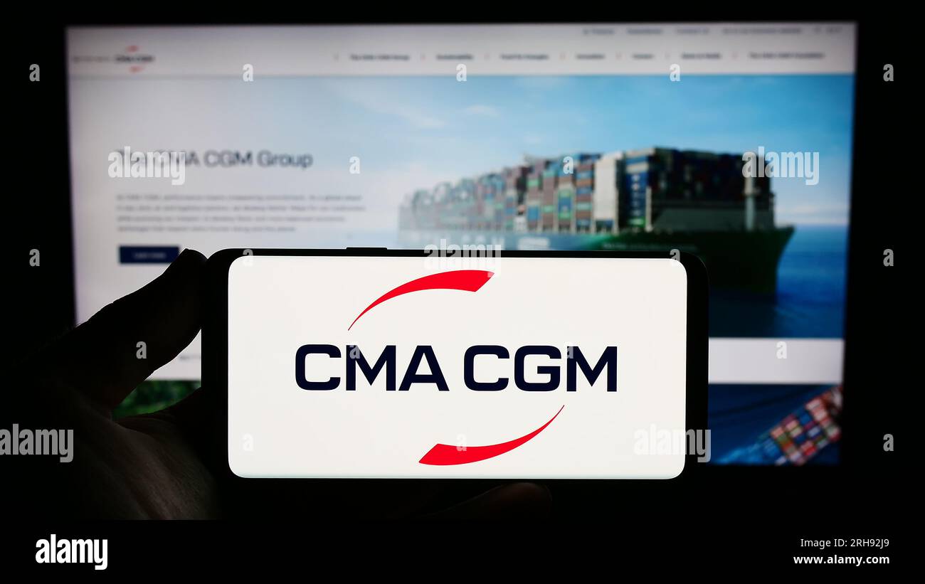 Persona che possiede uno smartphone con il logo della società di logistica francese CMA CGM S.A. sullo schermo di fronte al sito Web. Concentrarsi sul display del telefono. Foto Stock
