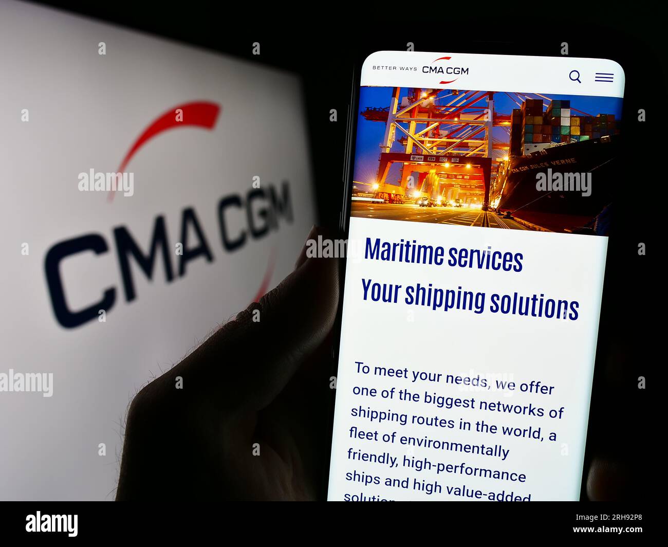 Persona in possesso di cellulare con pagina web della società di logistica francese CMA CGM S.A. sullo schermo davanti al logo. Concentrarsi sul centro del display del telefono. Foto Stock