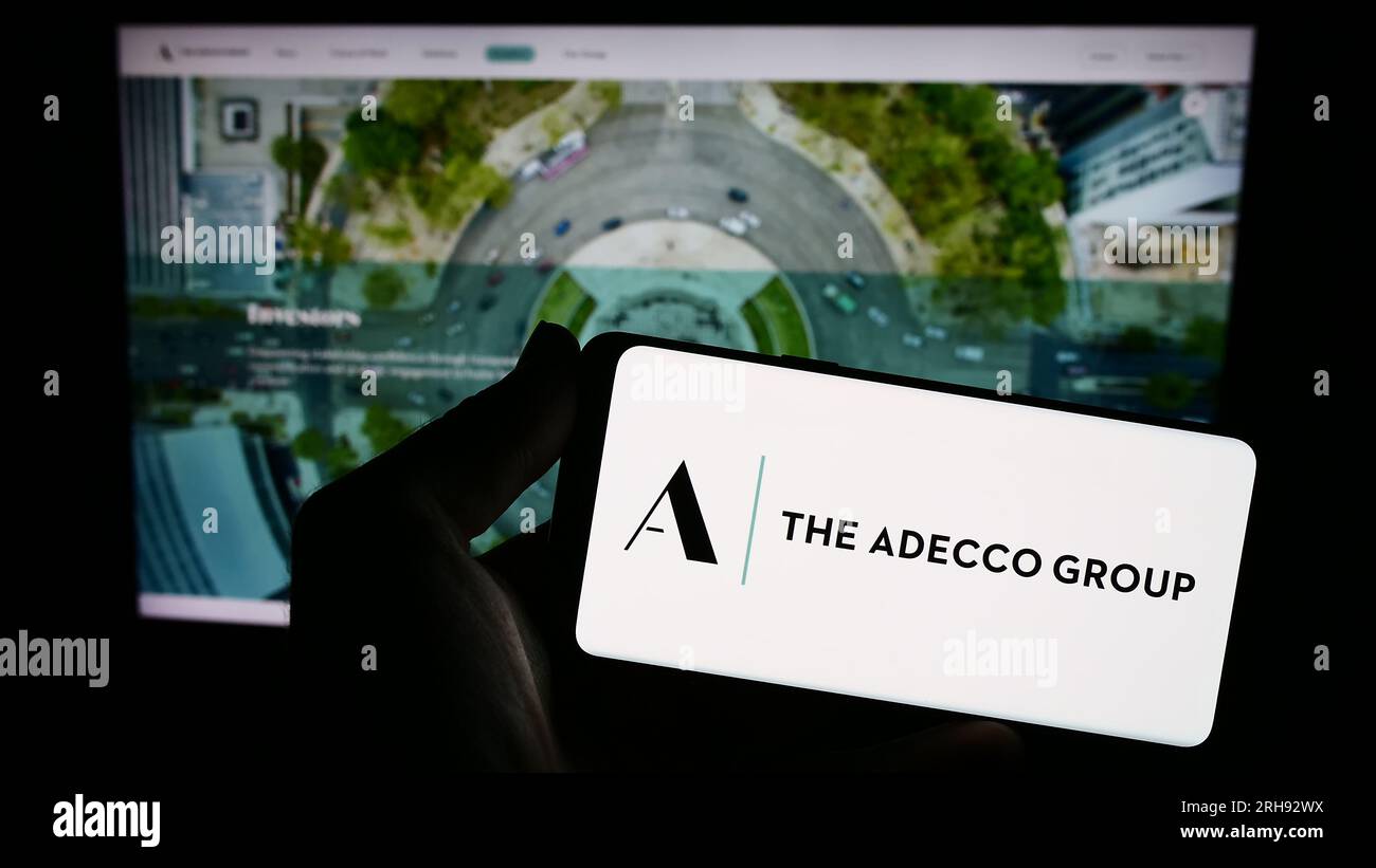 Persona che possiede uno smartphone con il logo della società delle risorse umane Adecco Group AG sullo schermo davanti al sito Web. Concentrarsi sul display del telefono. Foto Stock