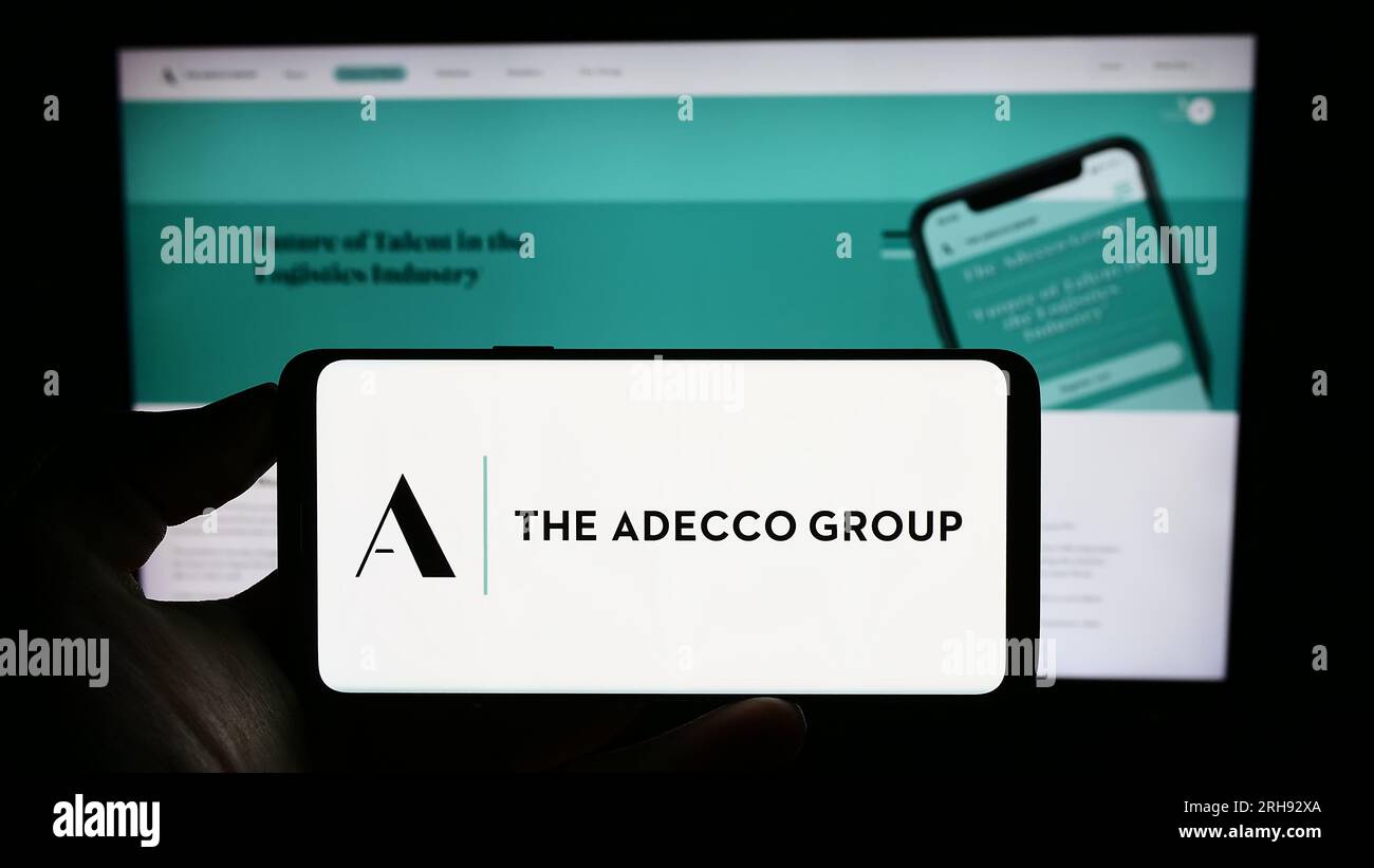 Persona che possiede un telefono cellulare con il logo della società delle risorse umane Adecco Group AG sullo schermo davanti alla pagina Web. Concentrarsi sul display del telefono. Foto Stock