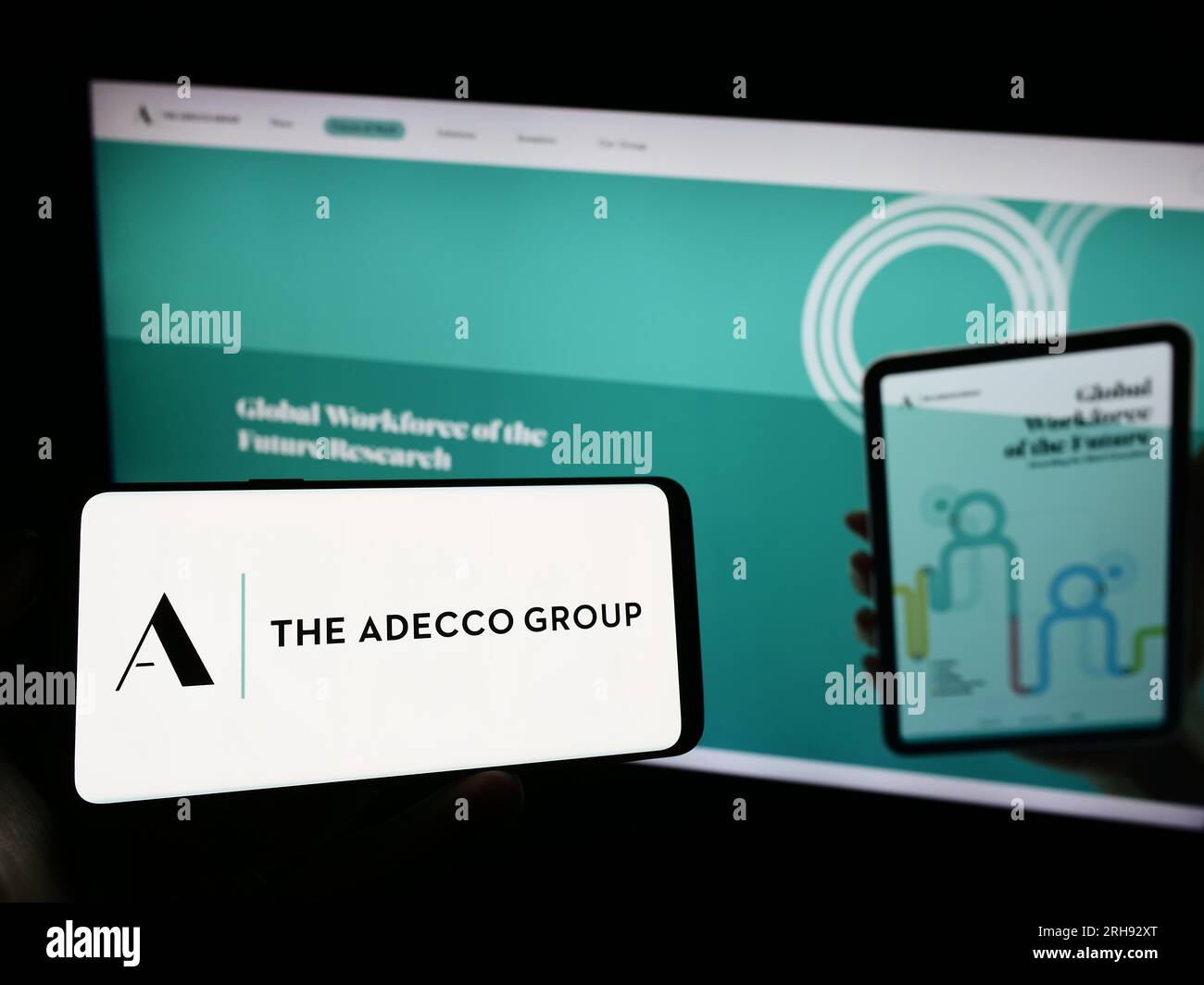 Persona che possiede il cellulare con il logo della società delle risorse umane Adecco Group AG sullo schermo davanti alla pagina Web aziendale. Concentrarsi sul display del telefono. Foto Stock