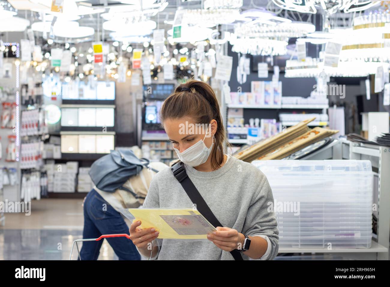 donna che indossa la maschera protettiva in piedi nel punto di vendita al dettaglio e legge le informazioni sulle merci. Foto Stock