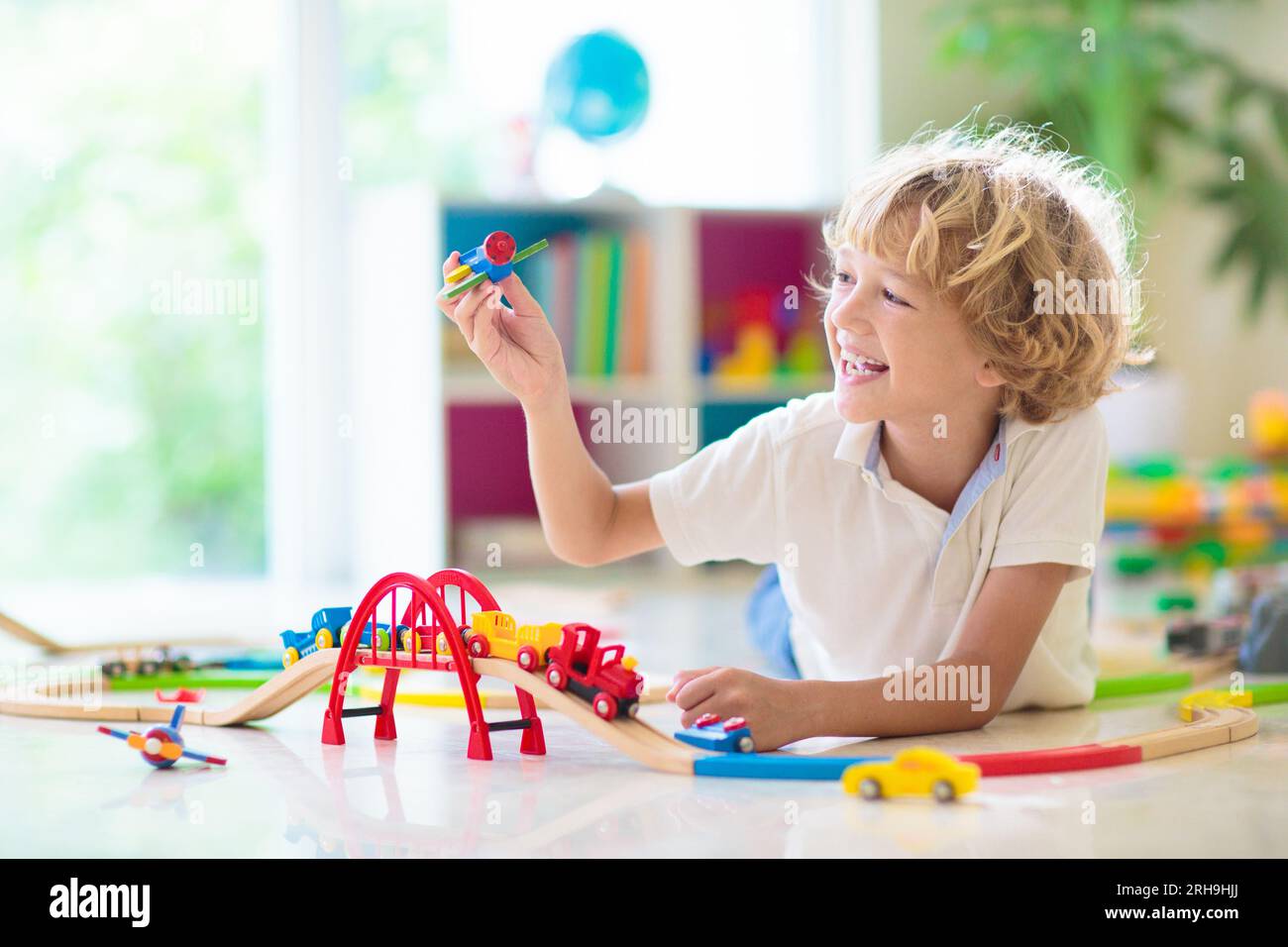 I bambini giocano con il treno giocattolo. Bambini che giocano con colorati treni in legno arcobaleno. Giocattoli per bambino. Costruzione di una strada ferroviaria per bambini in età prescolare a casa Foto Stock