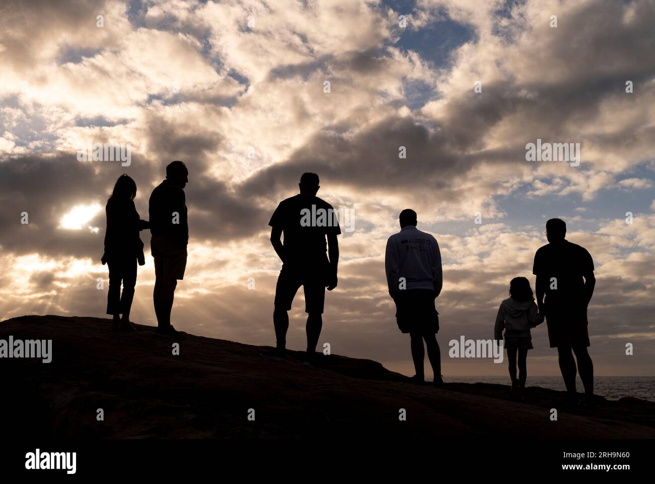 Sei sagome di persone con le spalle alla fotocamera che guardano un cielo al tramonto con nuvole dalle tonalità calde. Foto Stock