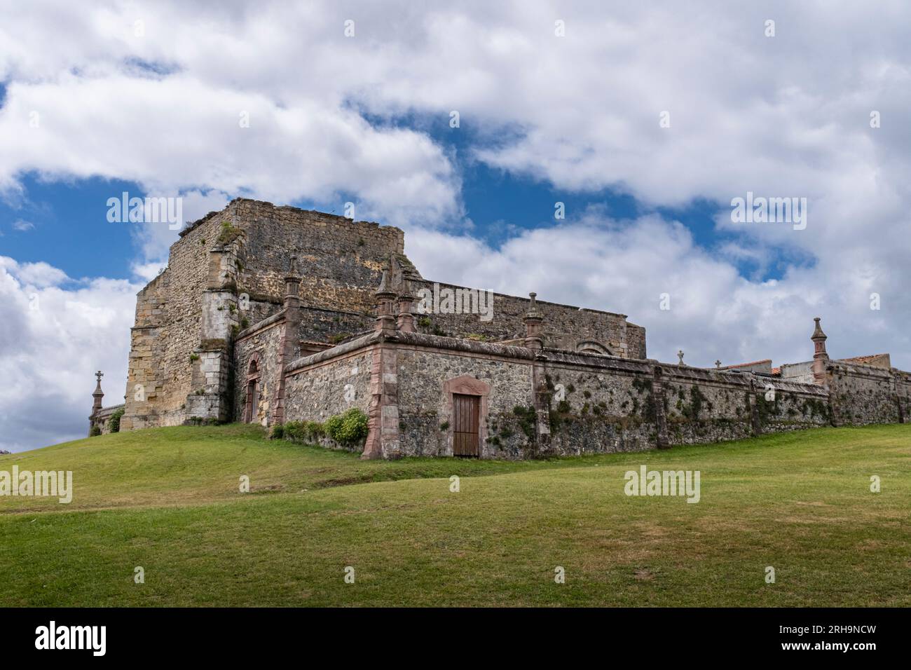 Vista delle rovine del cimitero gotico nella città cantabrica di Comillas, con un prato verde e un cielo blu con nuvole. Foto Stock