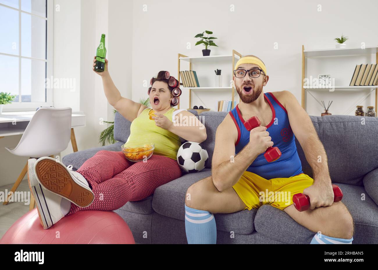 Donna grassa divertente con cibo e birra e uomo in forma con manichino che guarda il calcio in TV Foto Stock