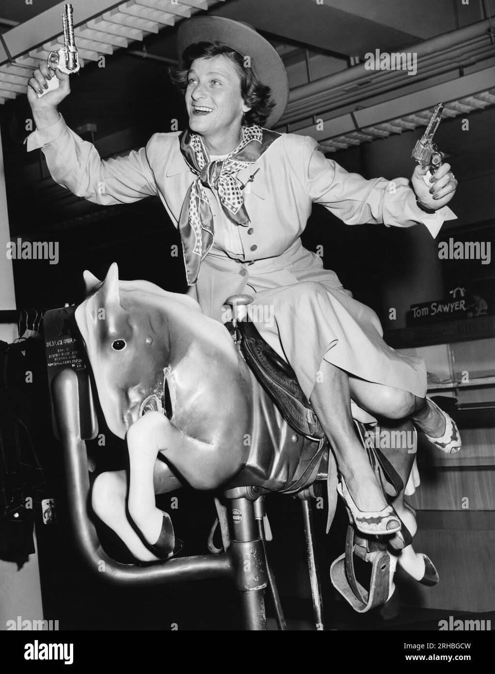 New Orleans, Louisiana: c. 1952 la star del golf Babe Didrikson si diverte con la sella e le pistole su un cavallo meccanico. Foto Stock