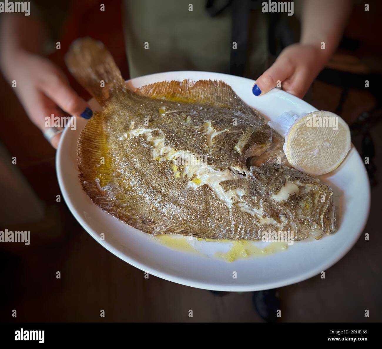 Primo piano di una donna che tiene un piatto con rombo cotto al momento e limone Foto Stock