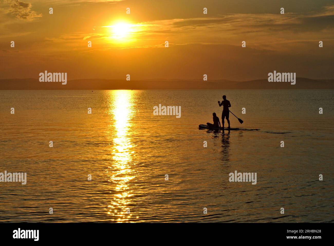 Due amanti del surf in paddleboard per ammirare il tramonto sul lago Balaton in Ungheria. Attività acquatiche durante le vacanze estive. Foto Stock