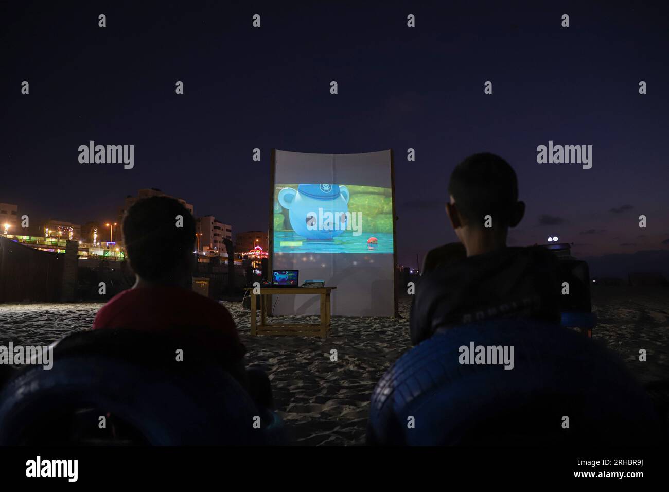 Gaza. 10 agosto 2023. I palestinesi guardano un film su un grande schermo installato su una spiaggia nella città di Gaza, il 10 agosto 2023. Entusiasti e grati per questa iniziativa di creare un cinema all'aperto gratuito, decine di spettatori di cinema locali di varie età si riunirono davanti al grande schermo dopo il tramonto. Guardavano film di diversi generi seduti su sedie convertite da pneumatici rotti riciclati. Crediti: Rizek Abdeljawad/Xinhua/Alamy Live News Foto Stock