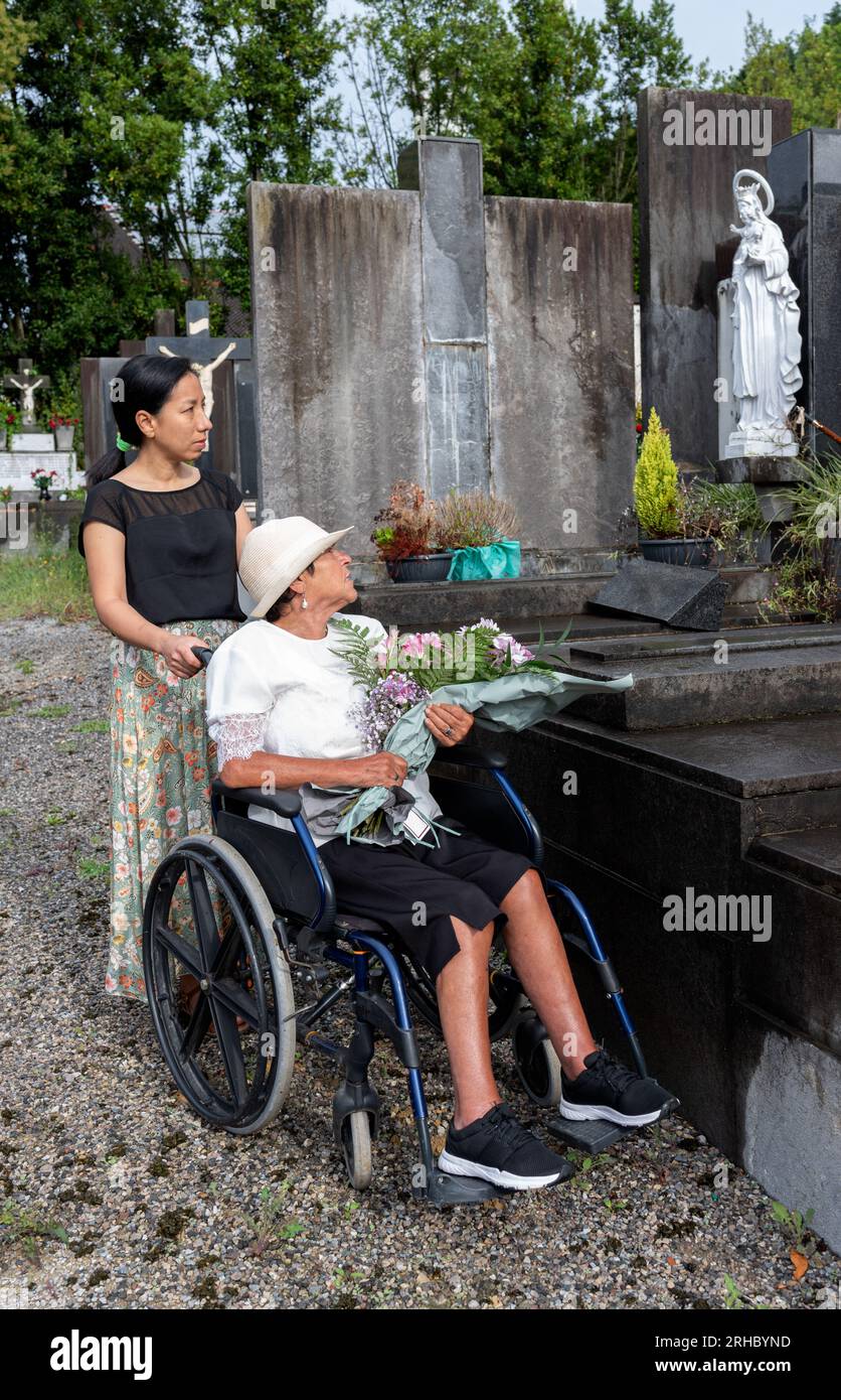 ragazza con donna disabile che porta fiori al cimitero Foto Stock