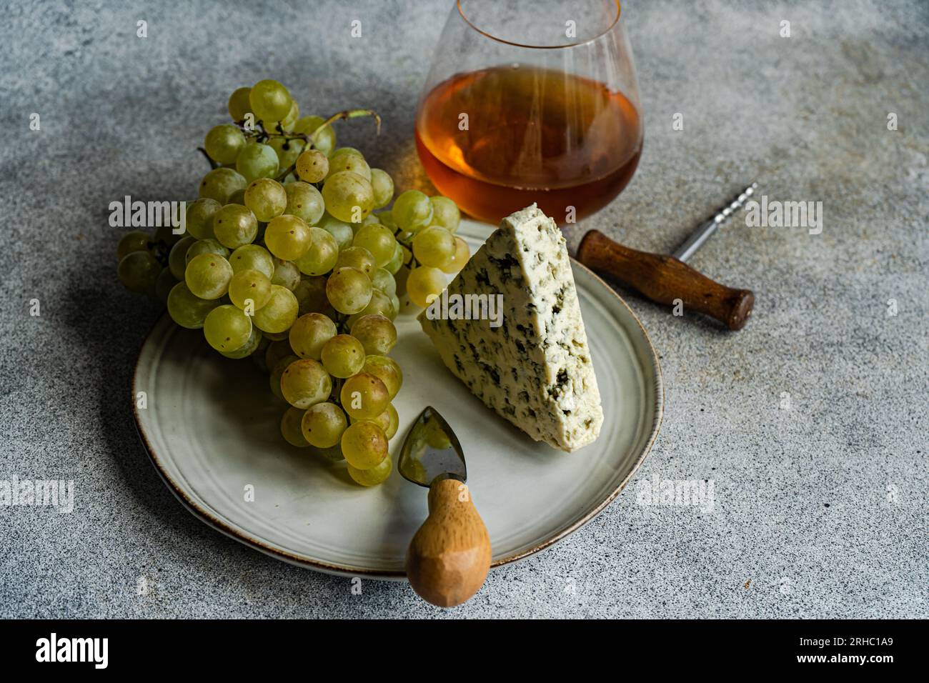 Piatto di formaggio blu con uva verde e un bicchiere di vino d'arancia Foto Stock