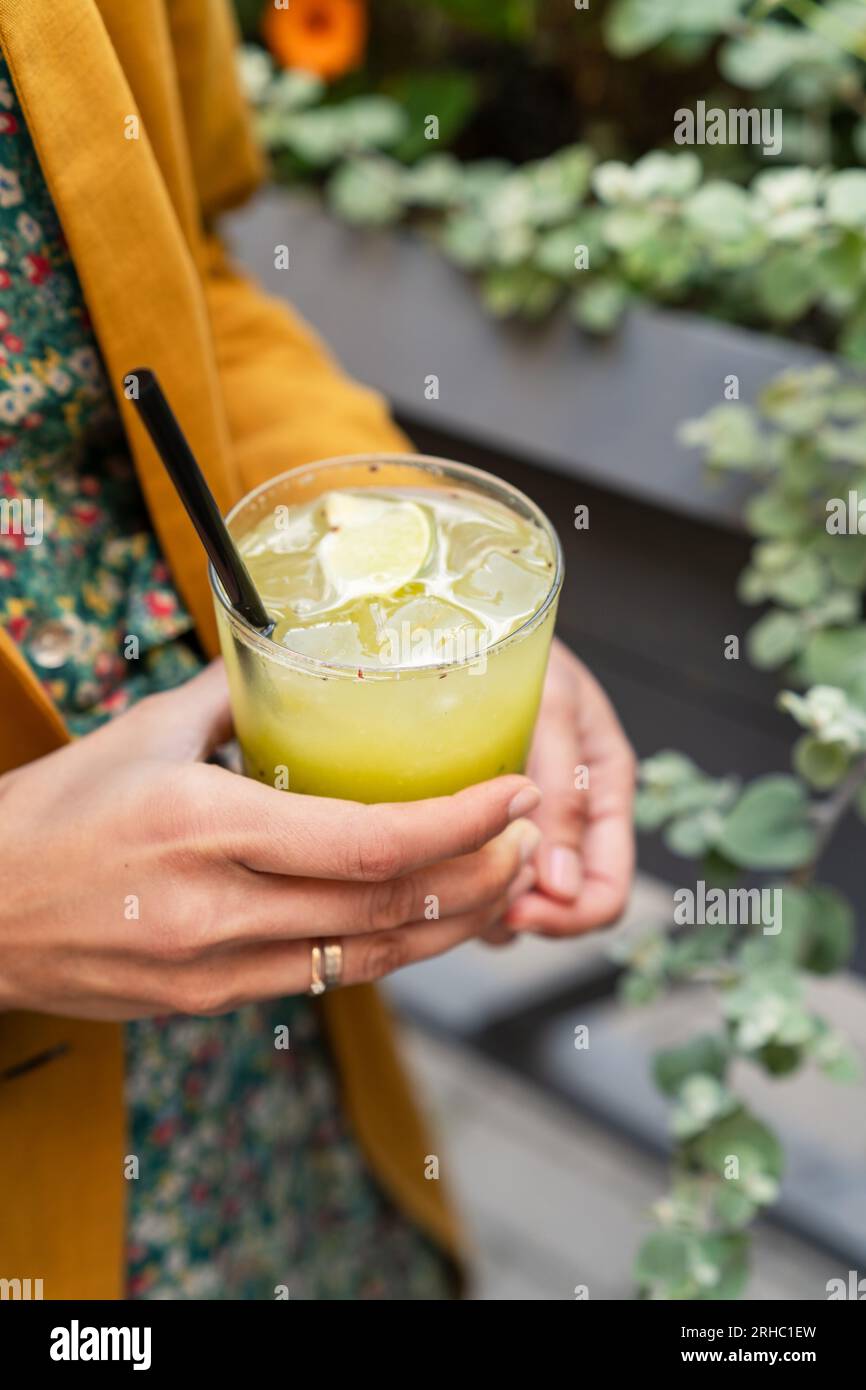 Primo piano di una donna all'aperto che tiene un kiwi verde e un cocktail di basilico Foto Stock