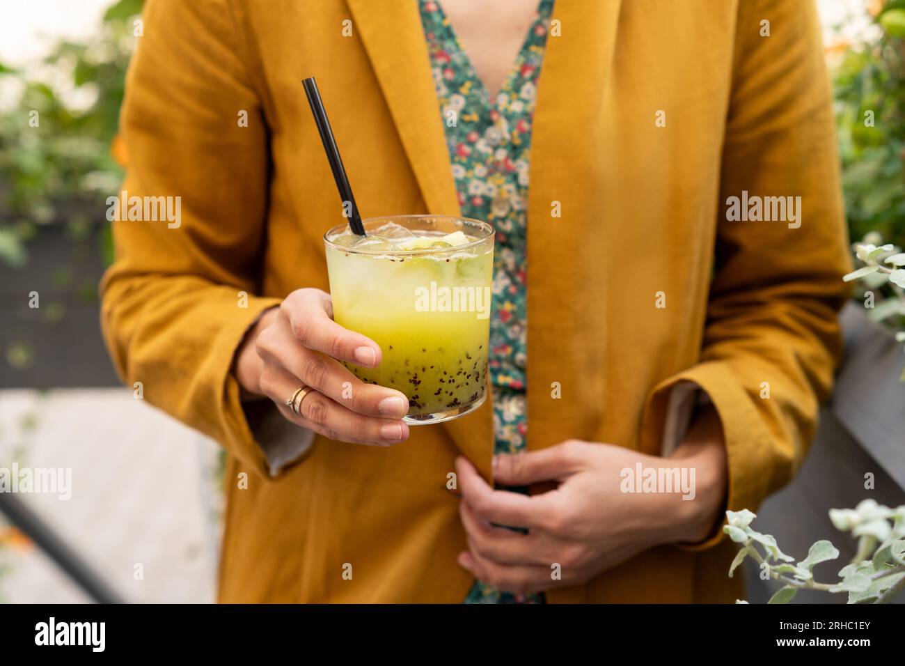 Primo piano di una donna all'aperto che tiene un kiwi verde e un cocktail di basilico Foto Stock