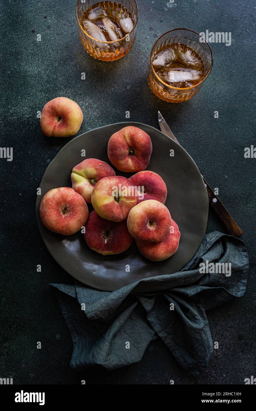 Due bicchieri di tè freddo accanto a una ciotola di pesche piatte Foto Stock