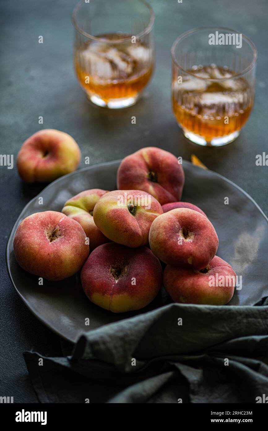 Due bicchieri di tè freddo accanto a una ciotola di pesche piatte Foto Stock