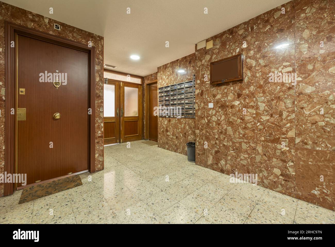 Portale di un edificio con accesso ad una casa al piano terra, porte in legno con pareti in marmo marrone e pavimenti in terrazzo chiaro Foto Stock